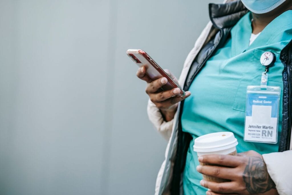 Soignant en tenue médicale consultant son smartphone en extérieur, illustrant l'infirmier libéral mobile entre deux visites.