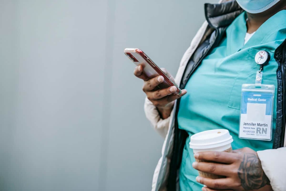 Soignant en tenue médicale consultant son smartphone en extérieur, illustrant l'infirmier libéral mobile entre deux visites.